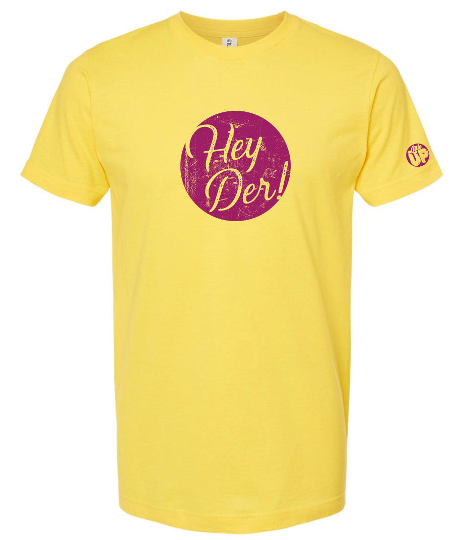 "Hey Der!" in script font, white on textured purple circle, on yellow t-shirt on white background