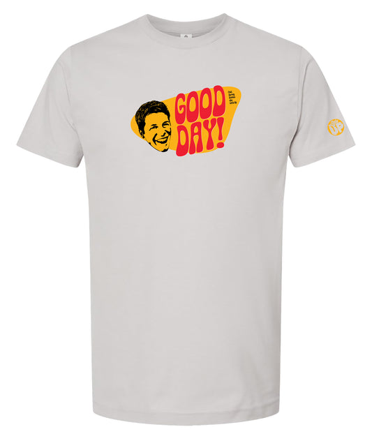 A light gray crewneck t-shirt featuring a retro graphic print on the chest with the text 'GOOD DAY!' in red and yellow, alongside a stylized yellow face illustration.