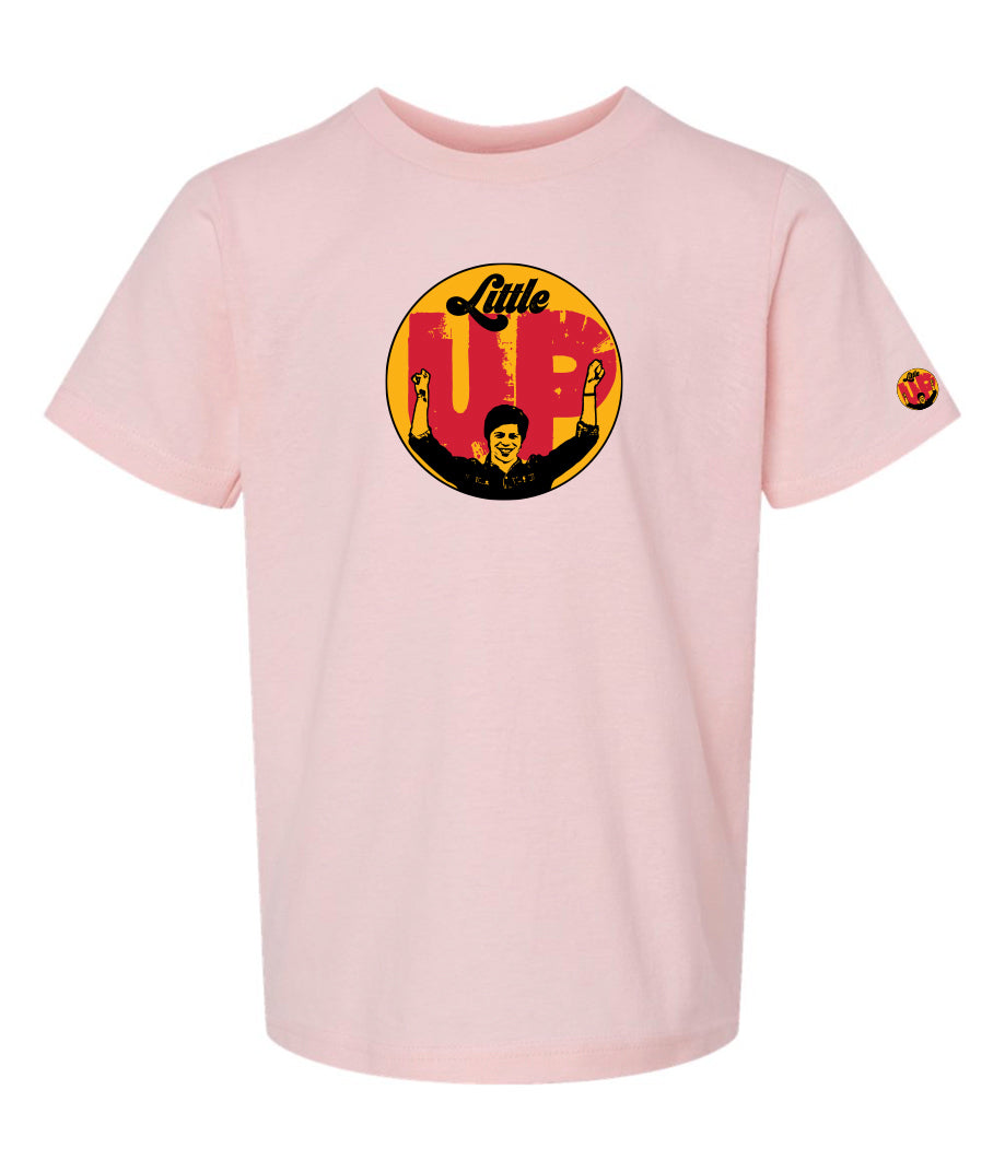 large circle with "Little" at the top in 70s script, "UP" large in red textured sans serif, illustration of young man smiling with arms raised illustration in black at the bottom, on pink youth t-shirt