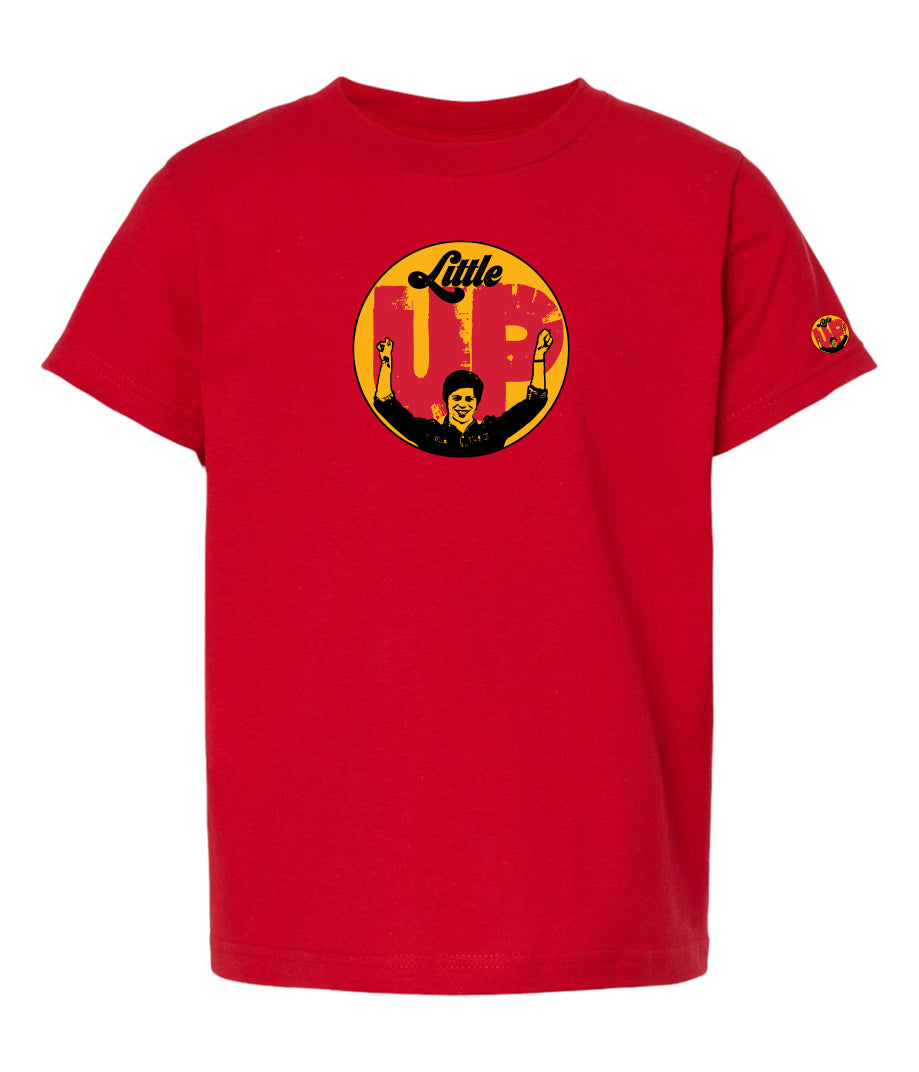 large circle with "Little" at the top in 70s script, "UP" large in red textured sans serif, illustration of young man smiling with arms raised illustration in black at the bottom, on red youth t-shirt