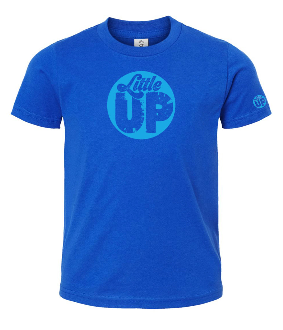 light blue circle logo with "Little" in the top third in textured seventies script and "UP" on the bottom ⅔ in modern sans serif textured font on blue youth t-shirt on white studio background