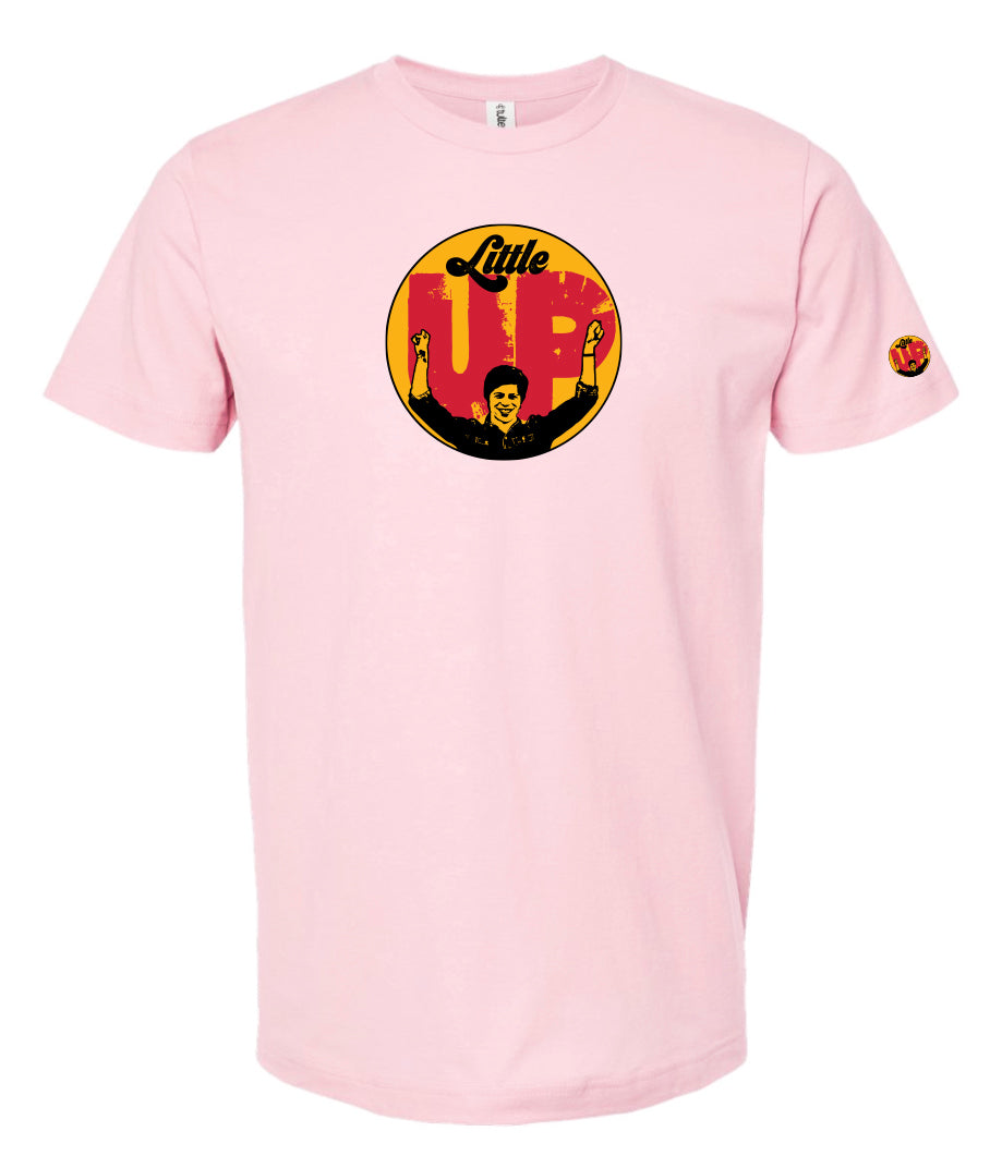 large circle with "Little" at the top in 70s script, "UP" large in red textured sans serif, illustration of young man smiling with arms raised illustration in black at the bottom, on pink t-shirt