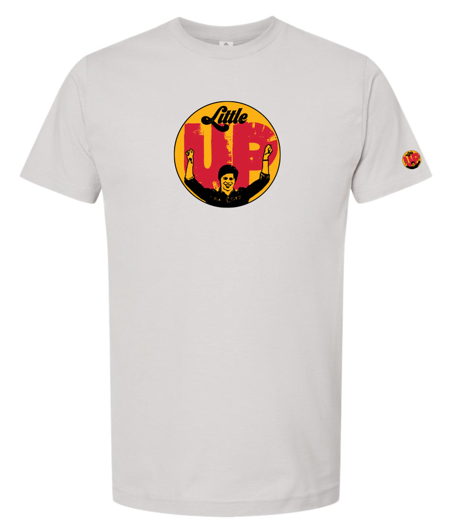 large circle with "Little" at the top in 70s script, "UP" large in red textured sans serif, illustration of young man smiling with arms raised illustration in black at the bottom, on light gray t-shirt