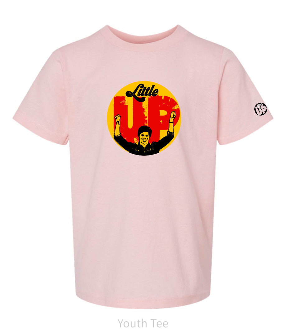 large circle with "Little" at the top in 70s script, "UP" large in red textured sans serif, illustration of young man smiling with arms raised illustration in black at the bottom, on pink youth t-shirt